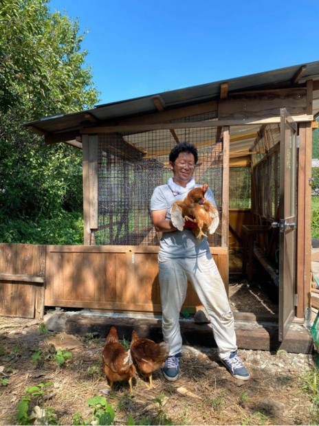 自分で建てた小屋の前で鶏を抱きながら記念撮影